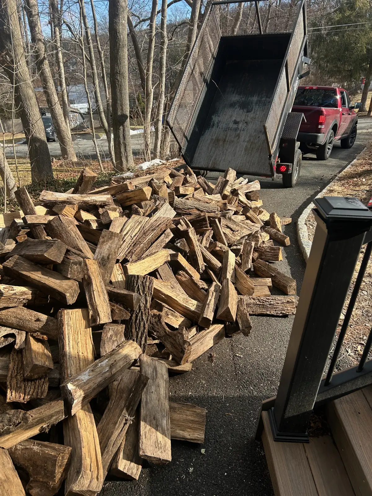 A dump trailer tipping a load of firewood onto a driveway on a winter day